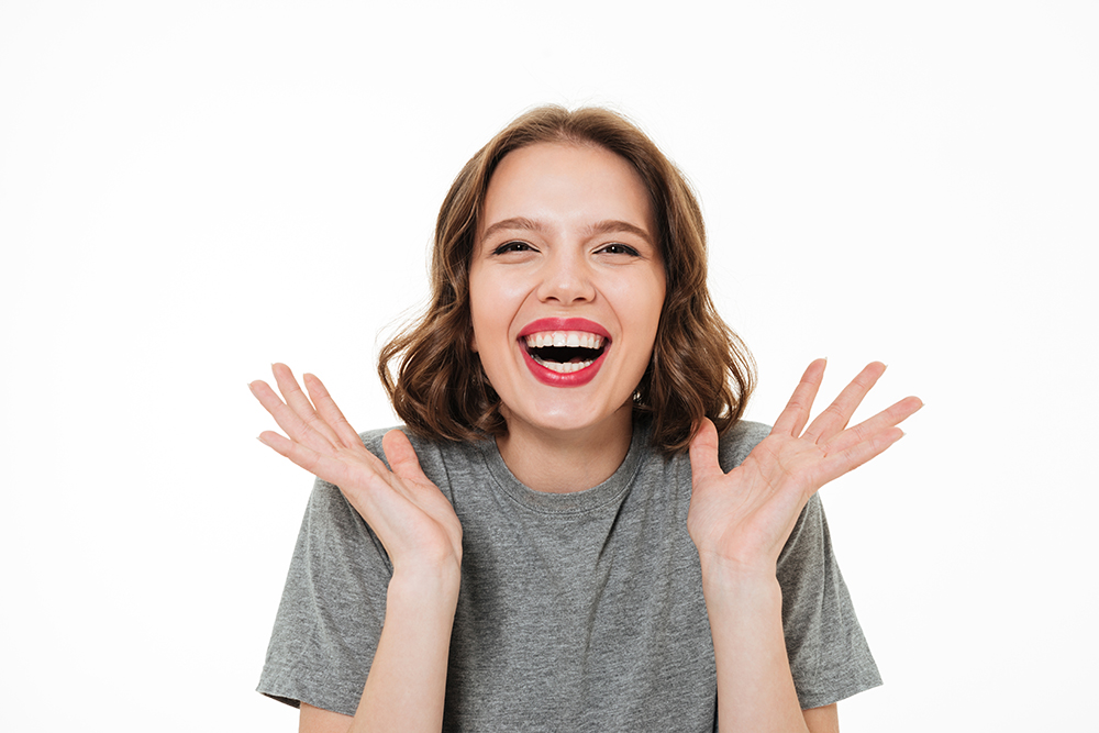 Close up portrait of an excited smiling woman with make-up laughing at camera and gesturing with hands isolated over white background