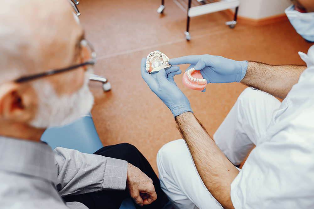 Handsome old man talking to the dendist. Two men in the dentist's office. The doctor shows the patient dentures